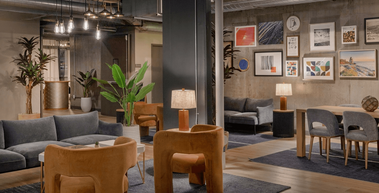 Lounge at The Loom Hotel with burnt-orange armchairs, grey sofas, potted palms and a gallery wall of framed art